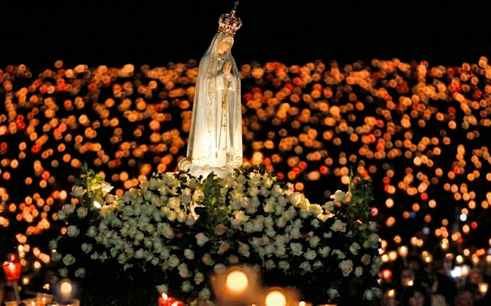 Candlelight procession at Fatima with statue surrounded by flowers.