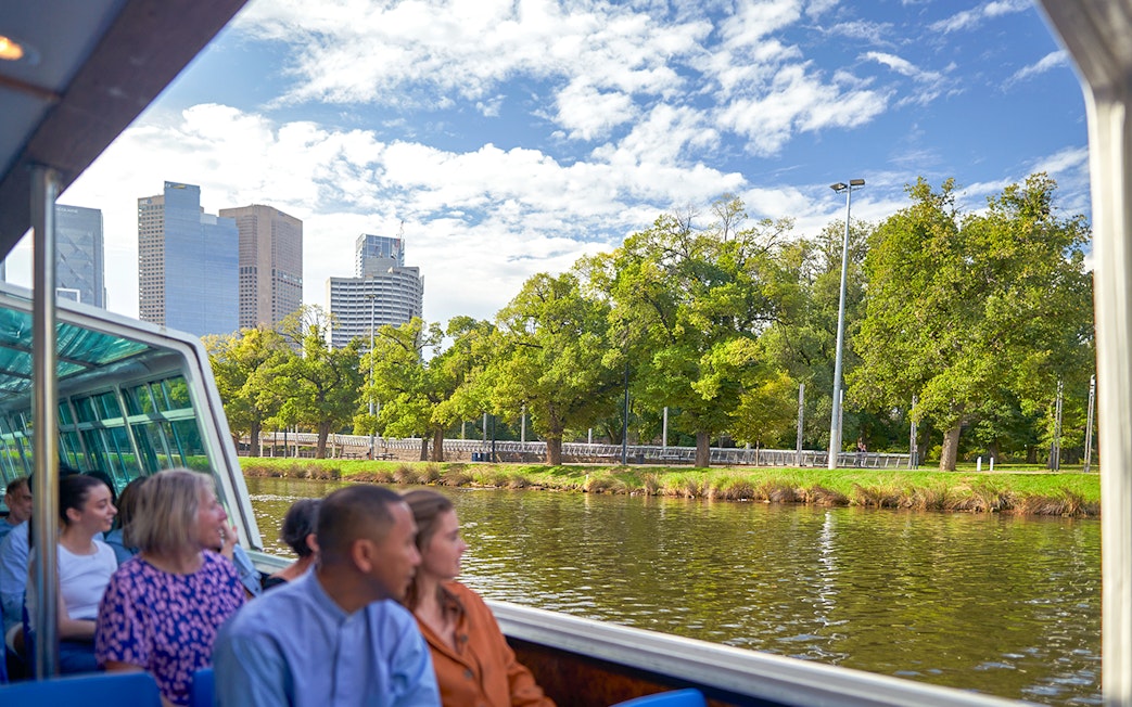 Guests enjoying Melbourne River Cruise with city skyline and greenery.