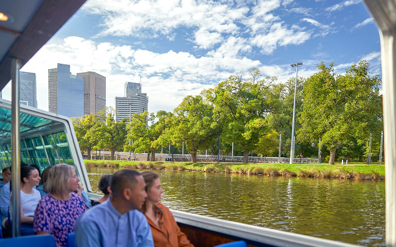 Guests enjoying Melbourne River Cruise with city skyline and greenery.