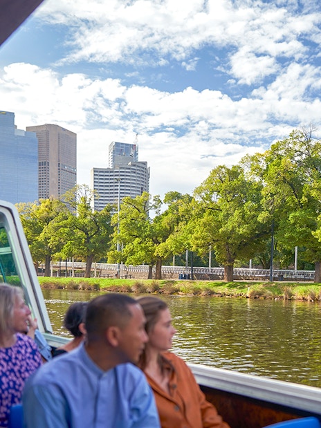 Guests enjoying Melbourne River Cruise with city skyline and greenery.