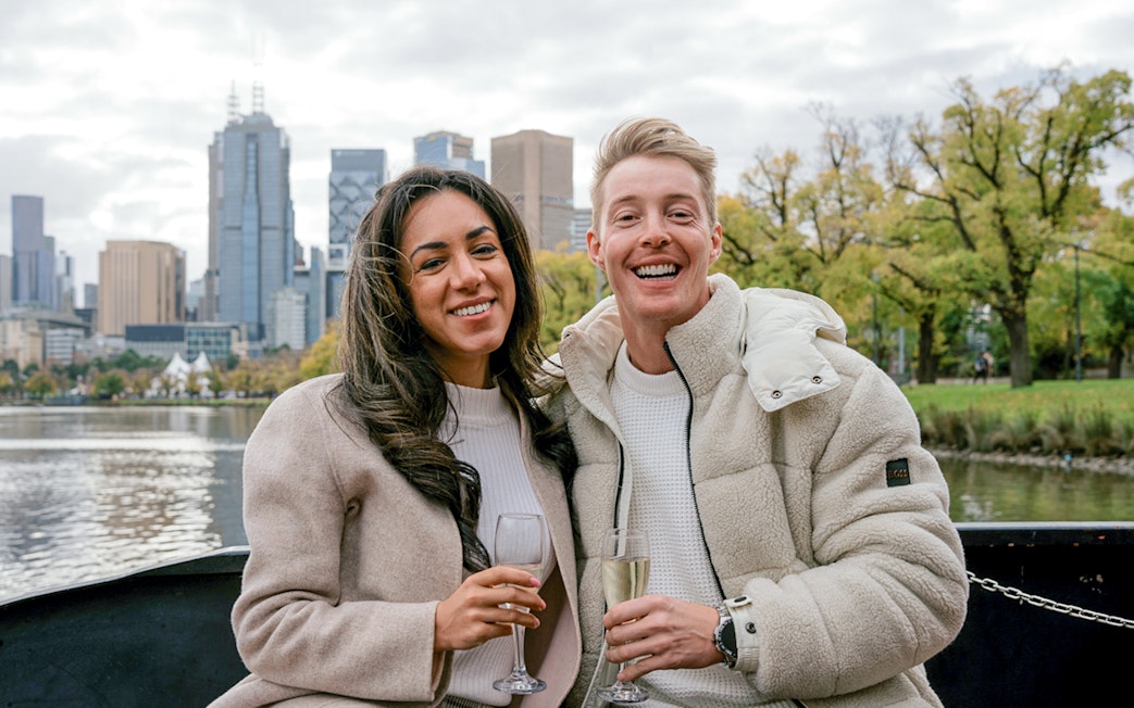 Couple enjoying champagne on a Melbourne brunch cruise with city skyline in background.