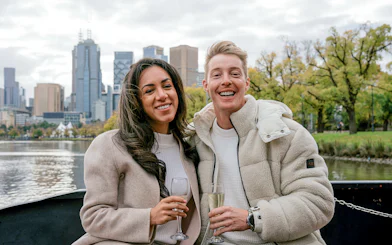 Couple enjoying champagne on a Melbourne brunch cruise with city skyline in background.