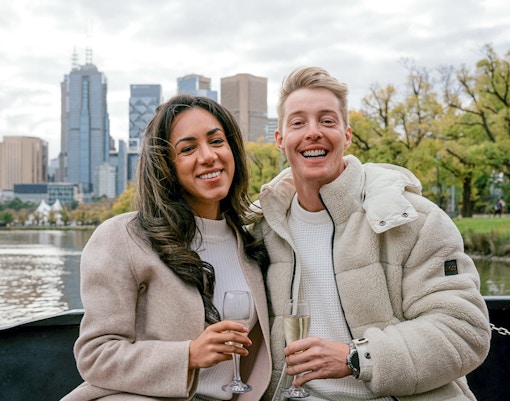 Couple enjoying champagne on a Melbourne brunch cruise with city skyline in background.