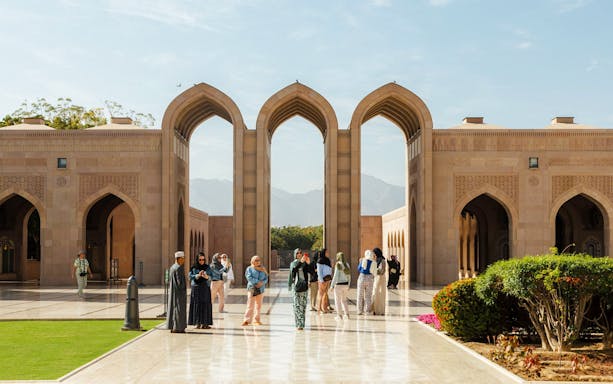 Tourists exploring courtyard of Royal Opera House Muscat with arches and gardens.