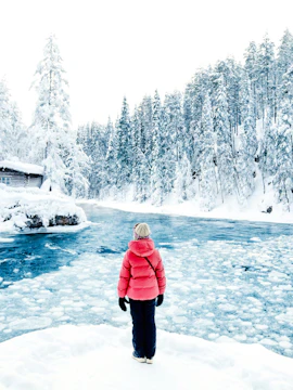 Person standing by a frozen river in Lapland Winter Park, surrounded by snow-covered trees.