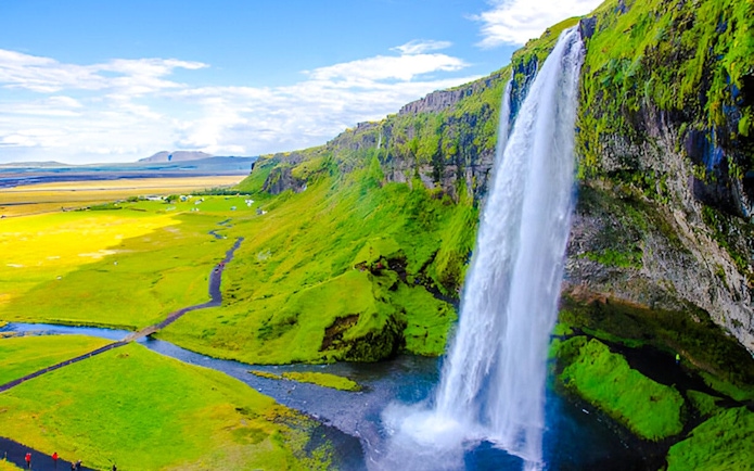 Guests walking near Skógafoss waterfall in Iceland, surrounded by lush green landscape.