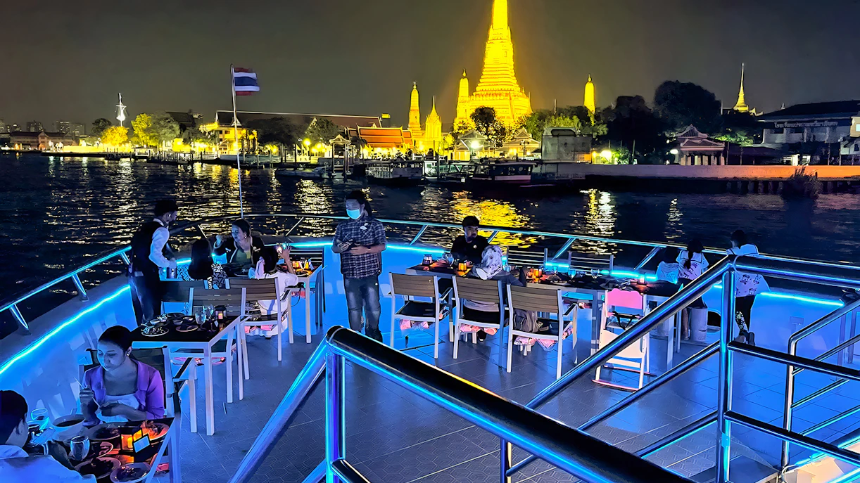 Riverside dinner cruise with buffet and live performances near illuminated Wat Arun, Bangkok.