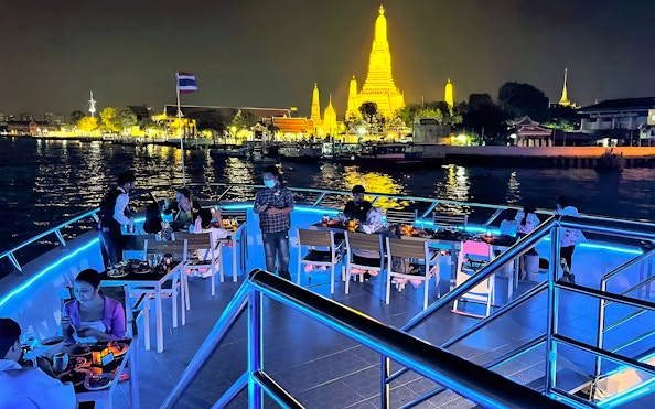 Riverside dinner cruise with buffet and live performances near illuminated Wat Arun, Bangkok.