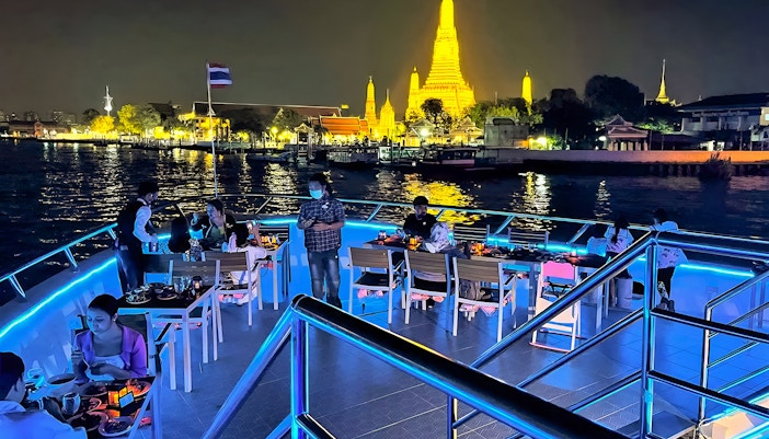 Riverside dinner cruise with buffet and live performances near illuminated Wat Arun, Bangkok.