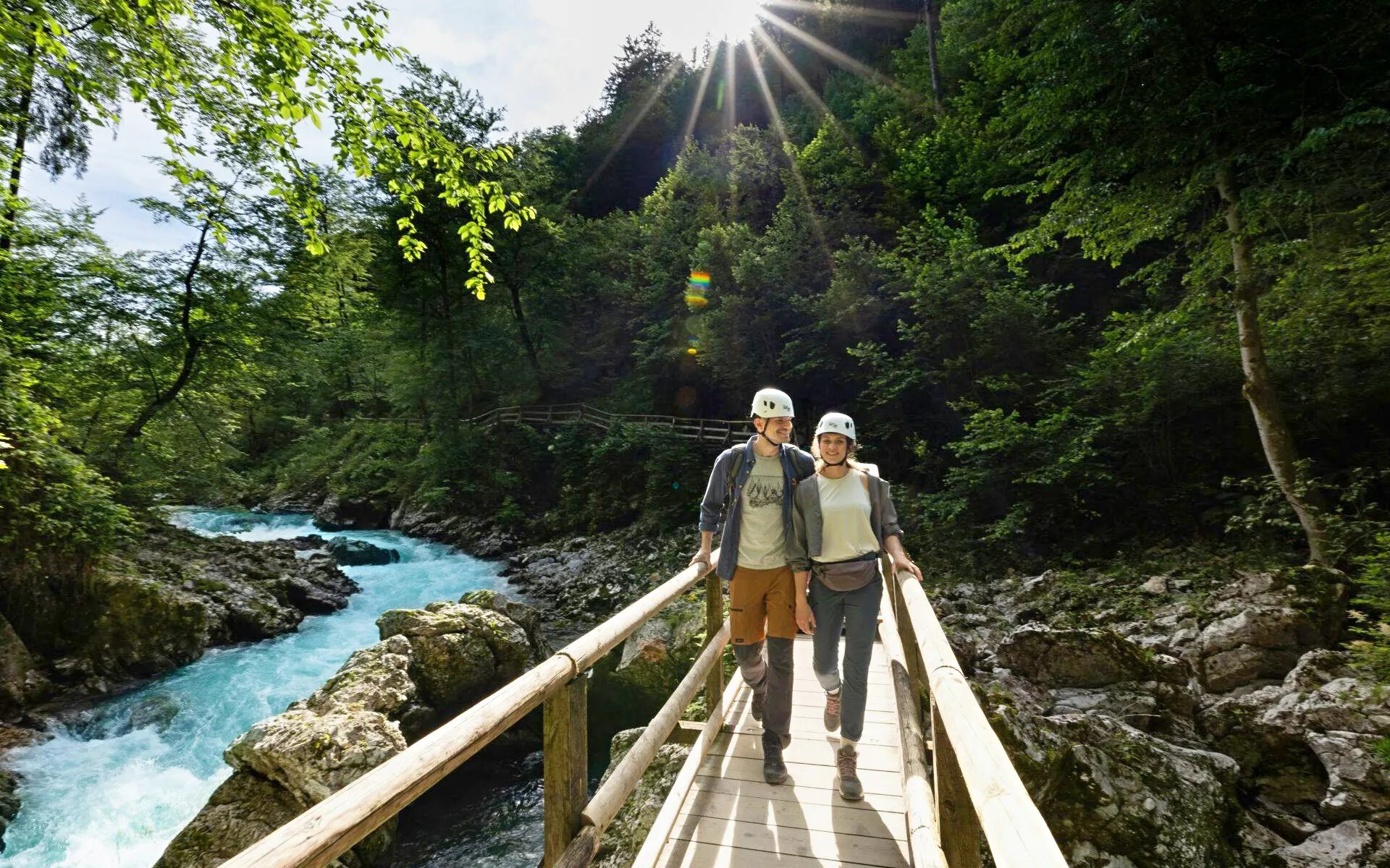 Couple walking on a wooden bridge over Vintgar Gorge, Slovenia, surrounded by lush greenery.