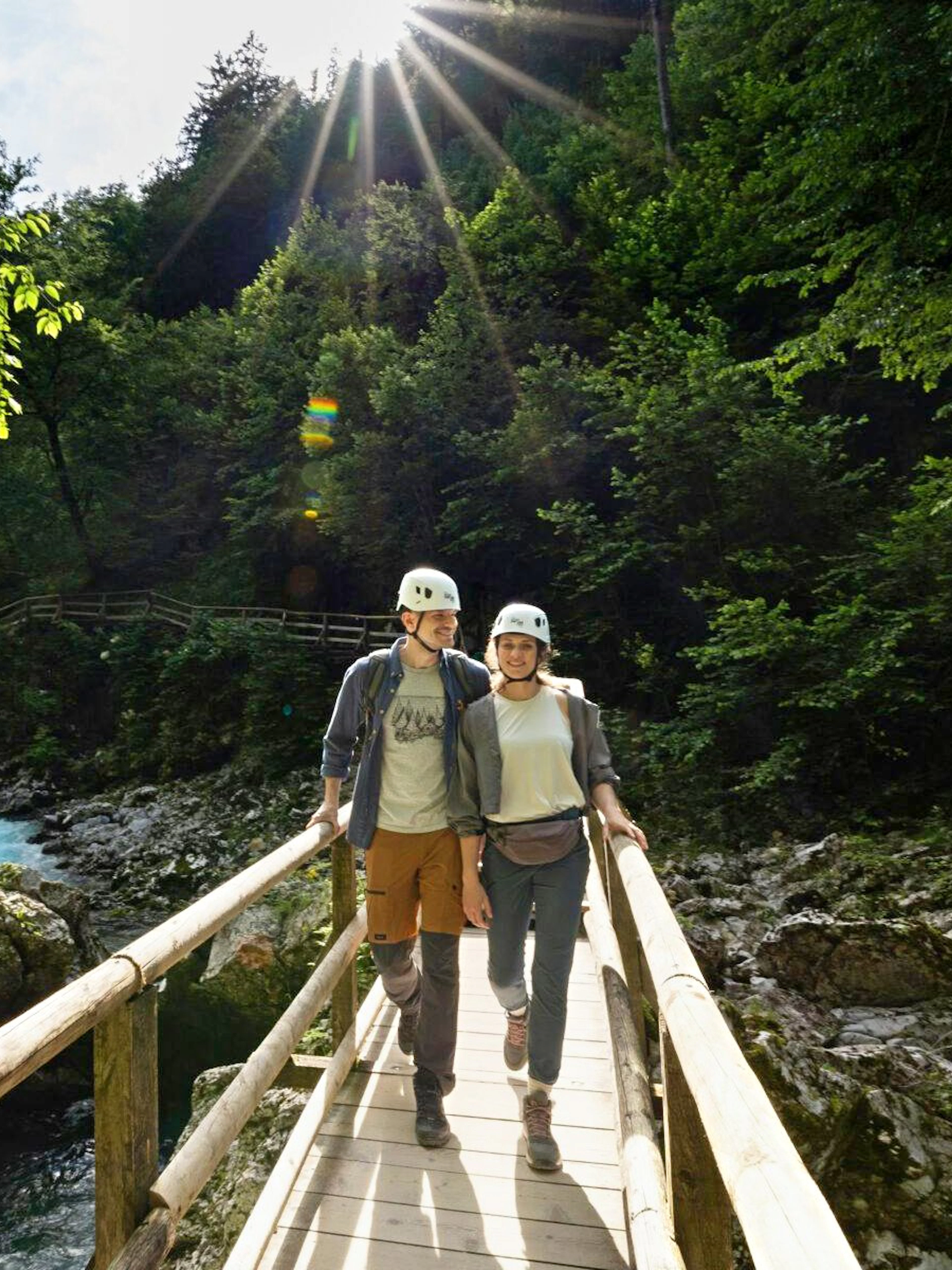 Couple walking on a wooden bridge over Vintgar Gorge, Slovenia, surrounded by lush greenery.