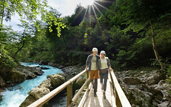 Couple walking on a wooden bridge over Vintgar Gorge, Slovenia, surrounded by lush greenery.