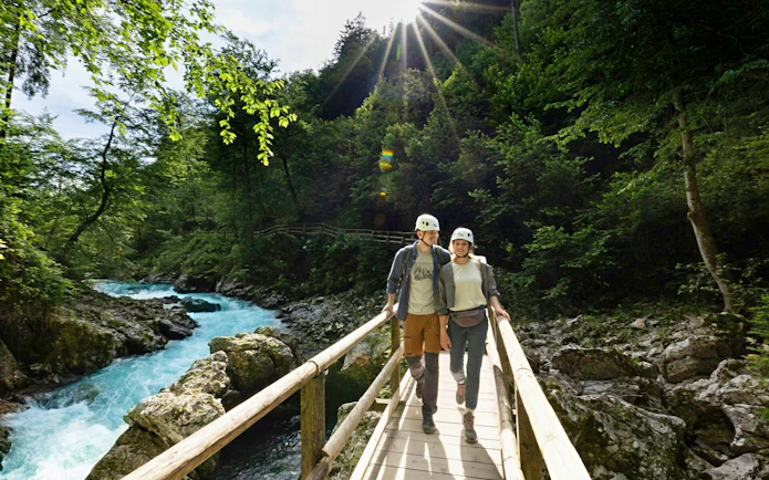 Couple walking on a wooden bridge over Vintgar Gorge, Slovenia, surrounded by lush greenery.