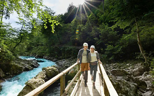 Couple walking on a wooden bridge over Vintgar Gorge, Slovenia, surrounded by lush greenery.
