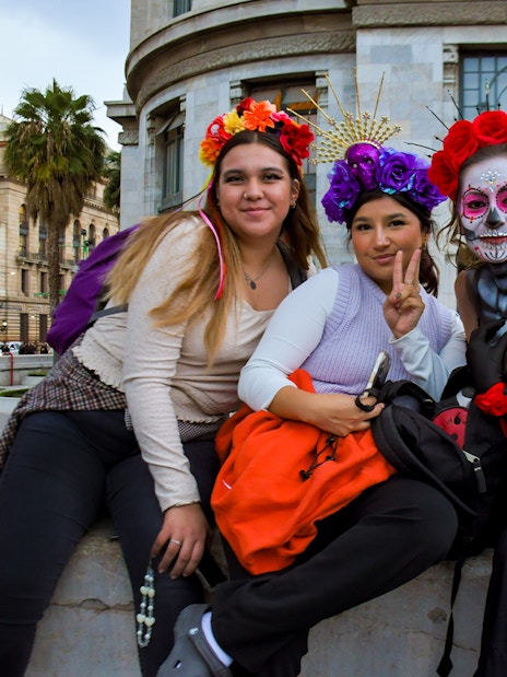 Tourists in traditional Day of the Dead attire at a parade in Mexico City.