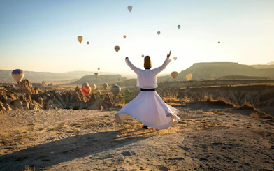 Whirling dervish performing in Cappadocia with hot air balloons in the background.