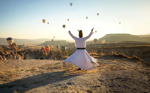 Whirling dervish performing in Cappadocia with hot air balloons in the background.