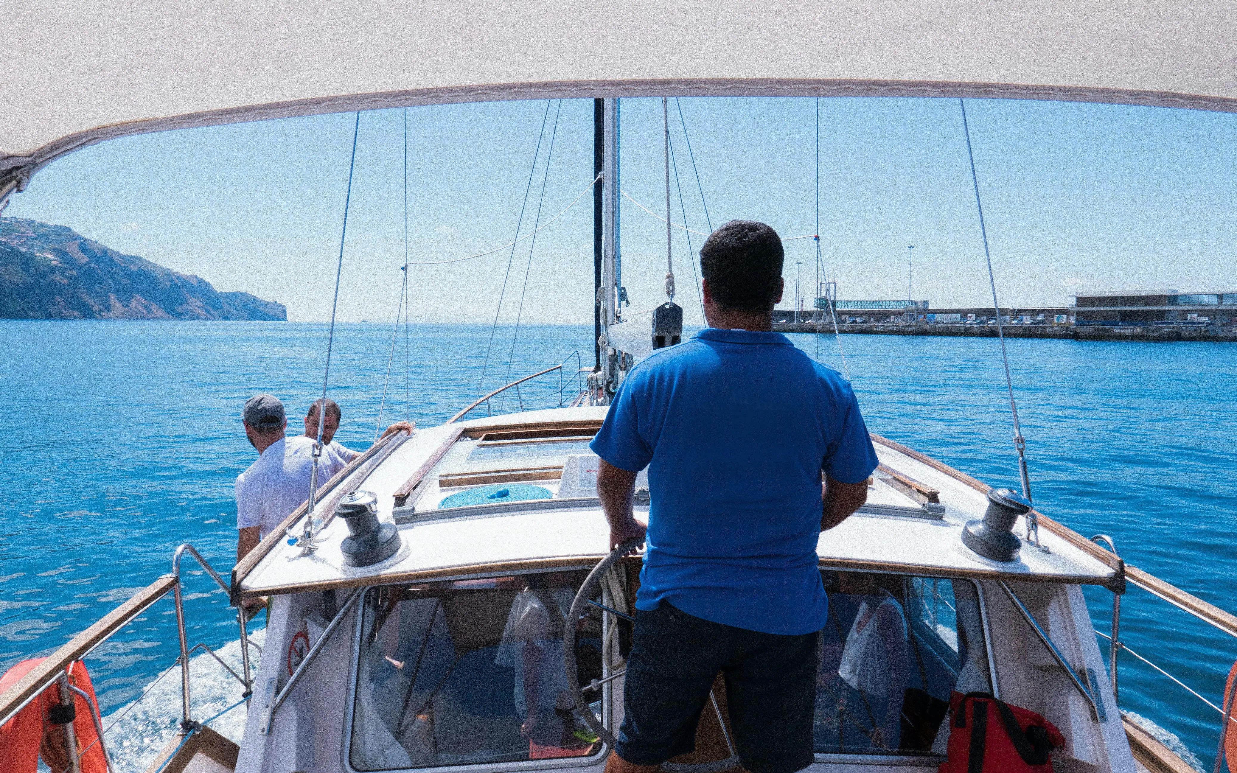 Catamaran sailing from Funchal with crew, ocean view and distant coastline.