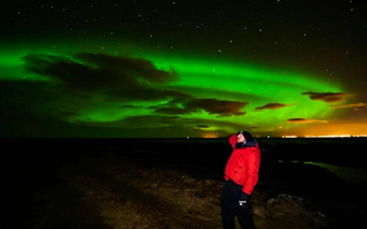 Northern Lights over Reykjavik with person in red jacket on Super Jeep tour.