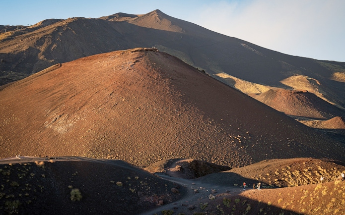 Mount Etna's volcanic landscape at sunset with hikers on the trail.