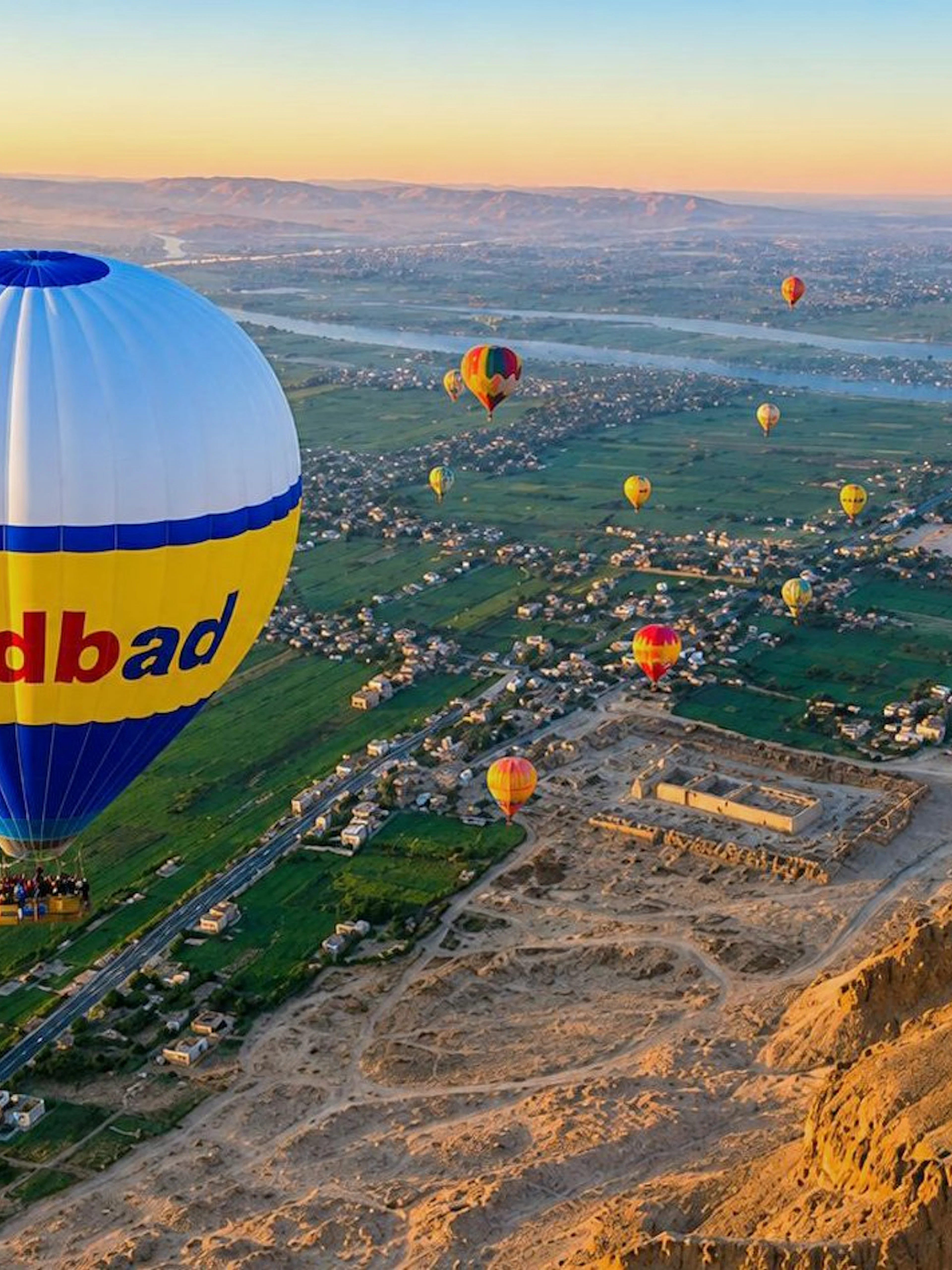 Hot air balloons over Luxor's landscape at sunrise, featuring the Nile River and desert.