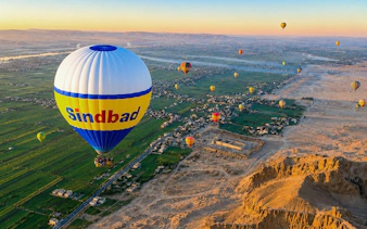 Hot air balloons over Luxor's landscape at sunrise, featuring the Nile River and desert.