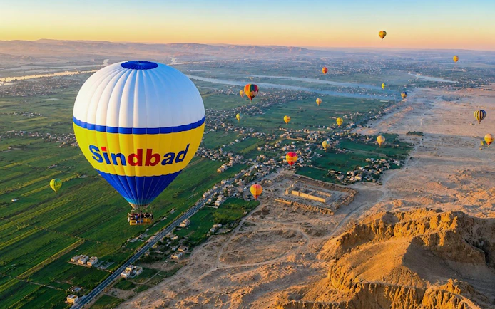Hot air balloons over Luxor's landscape at sunrise, featuring the Nile River and desert.