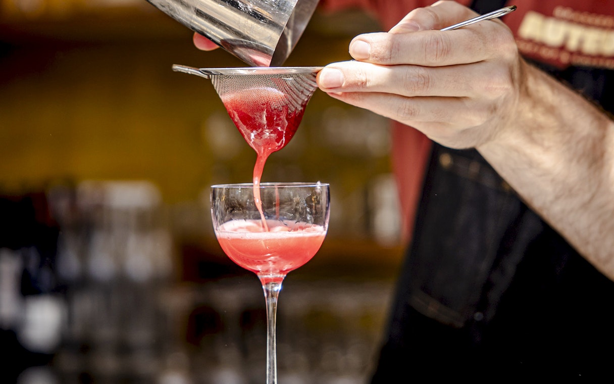 Cocktail waiter straining red drink into glass at Brasserie Auteuil.