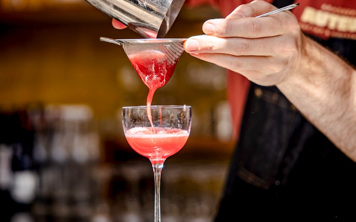 Cocktail waiter straining red drink into glass at Brasserie Auteuil.