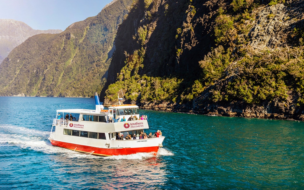 Cruise boat on Milford Sound with passengers, surrounded by lush cliffs.