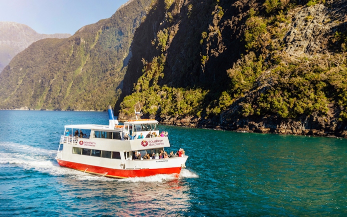 Cruise boat on Milford Sound with passengers, surrounded by lush cliffs.