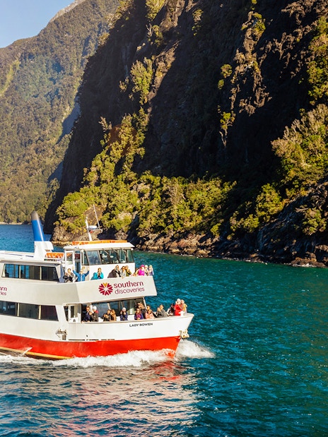 Cruise boat on Milford Sound with passengers, surrounded by lush cliffs.
