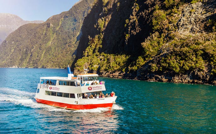 Cruise boat on Milford Sound with passengers, surrounded by lush cliffs.