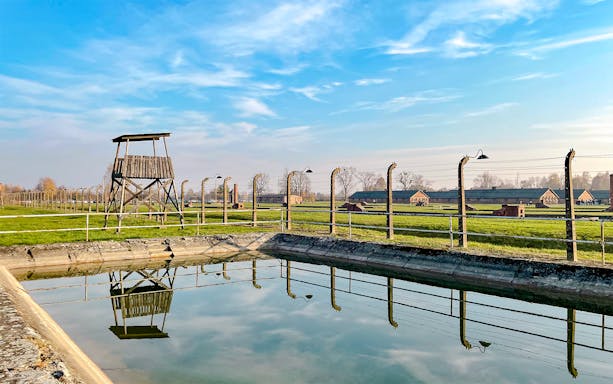 Guard tower and barbed wire fence at Auschwitz Birkenau, Poland, reflecting in water.