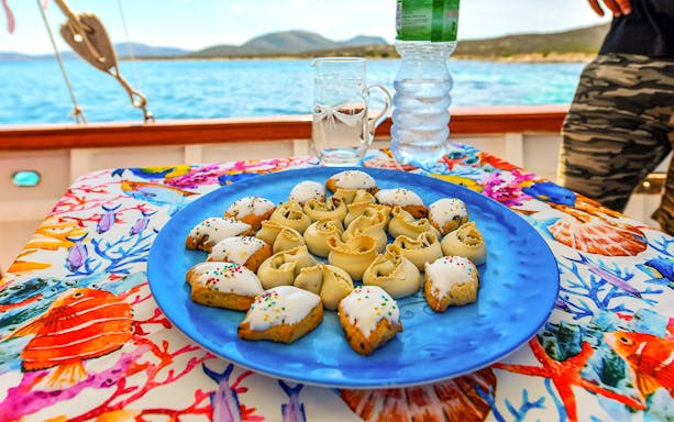 Pastries on a colorful tablecloth aboard a wooden sailboat near Asinara Island.