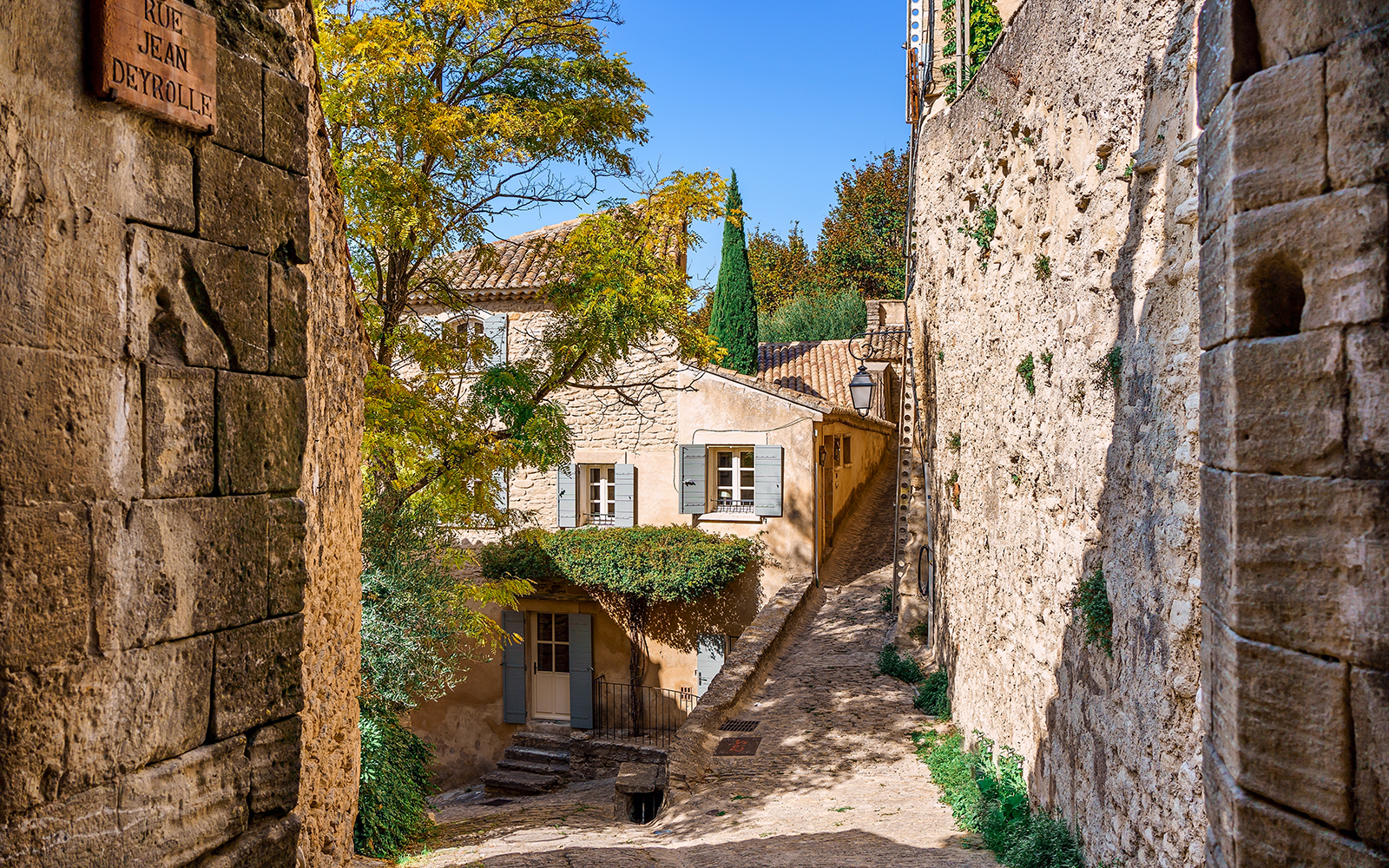 Stone alleyway in Sault, France, with rustic buildings and greenery.