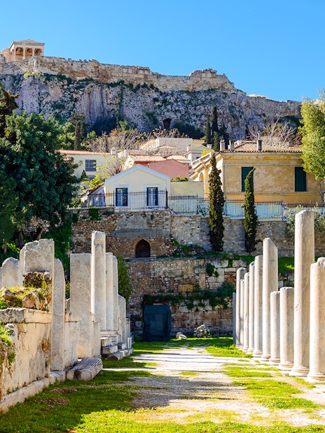 Ancient agora ruins with stone pillars in Athens, Greece, under the Acropolis.