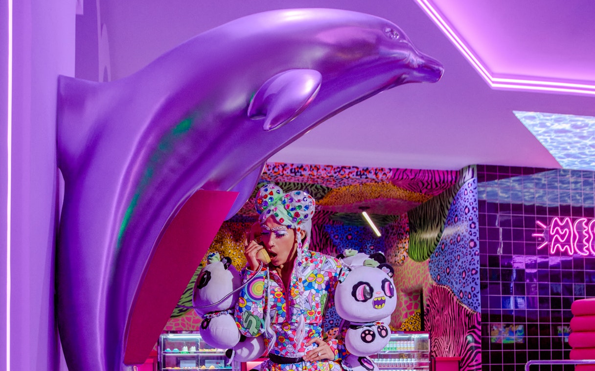 Person in colorful outfit at phone booth, Enchanted Carnival, Halloween Experience, House of Hype.