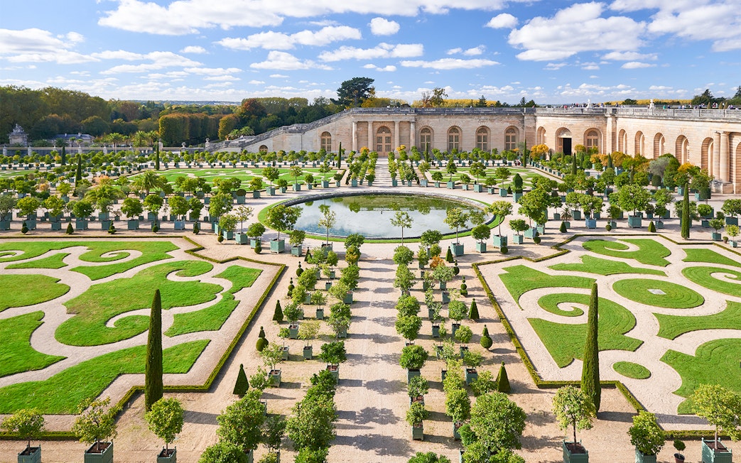 Versailles Gardens with manicured hedges and central fountain, France.