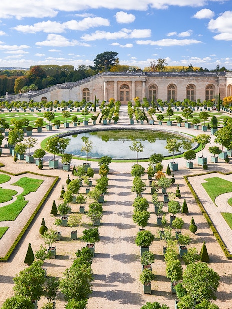 Versailles Gardens with manicured hedges and central fountain, France.