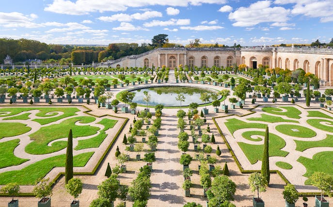 Versailles Gardens with manicured hedges and central fountain, France.