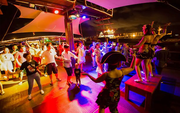Guests dancing on a lively pirate-themed dinner cruise at night.