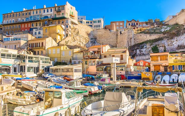 Boats docked in Marseille's sea district with colorful hillside buildings.