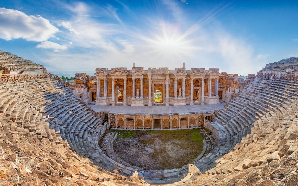 Amphitheater in ancient city of Hierapolis with stone seating and stage under a bright sky.