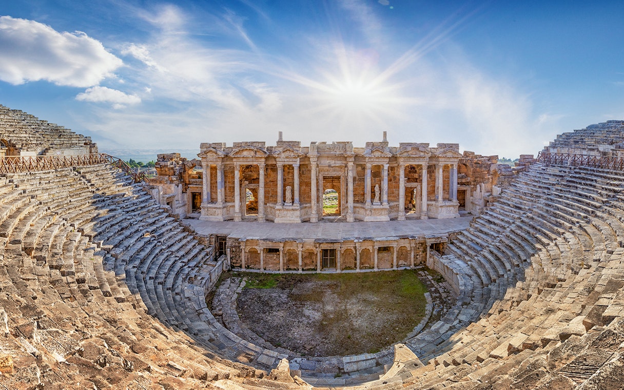 Amphitheater in ancient city of Hierapolis with stone seating and stage under a bright sky.
