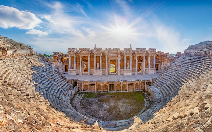 Amphitheater in ancient city of Hierapolis with stone seating and stage under a bright sky.