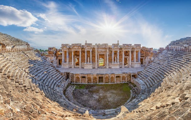Amphitheater in ancient city of Hierapolis with stone seating and stage under a bright sky.