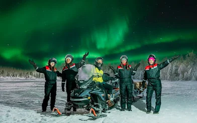 Group enjoying Northern Lights with sleigh ride in snowy landscape.