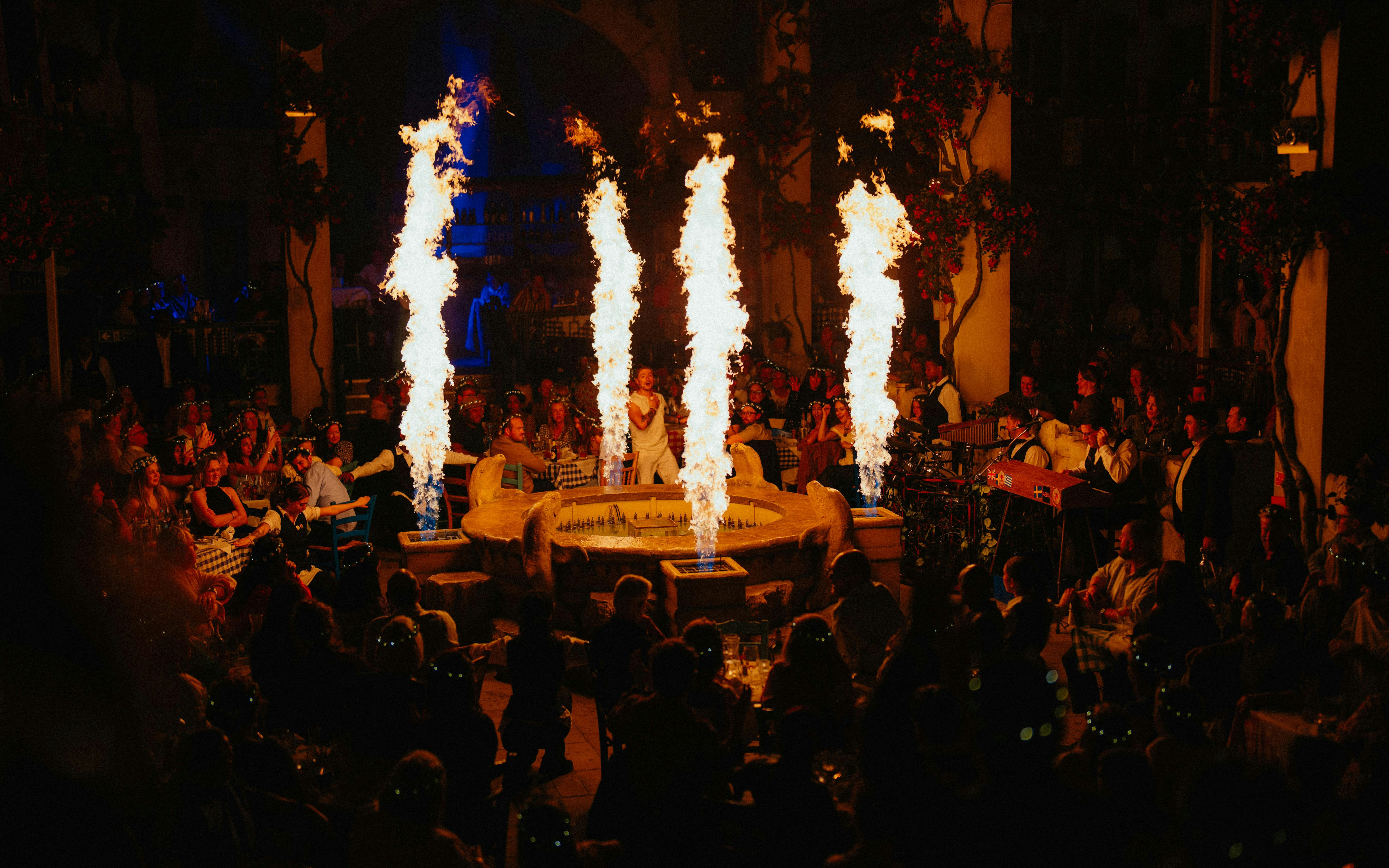 Audience enjoying Mamma Mia! The Party with performers and fire effects in a lively setting.