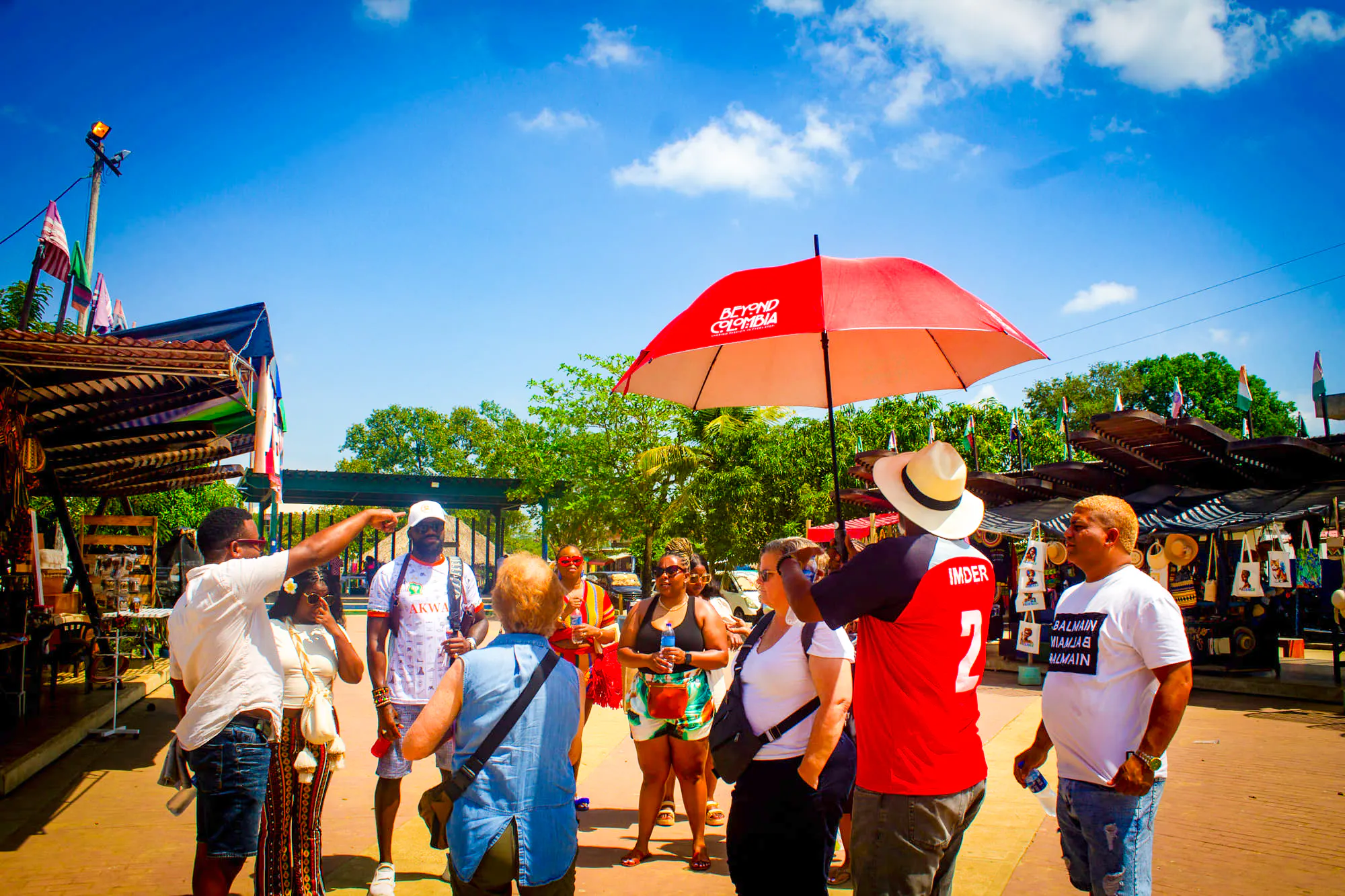 Tour group exploring San Basilio de Palenque market, Cartagena, with guide under red umbrella.